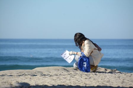 A Coastkeeper and Surfrider volunteer kneels on the beach during a cleanup.